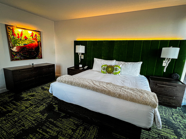 Guest bedroom with green headboard, white sheet bed with green pillow, and lighted fox painting at the Grand Bohemian Lodge in Greenville, SC