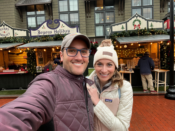 Greenville Christmas Market at the Grand Bohemian Lodge with Christine and Tom, a white brunette female and male in winter coats and hats, taking a selfie in front of outdoor market stalls for shopping