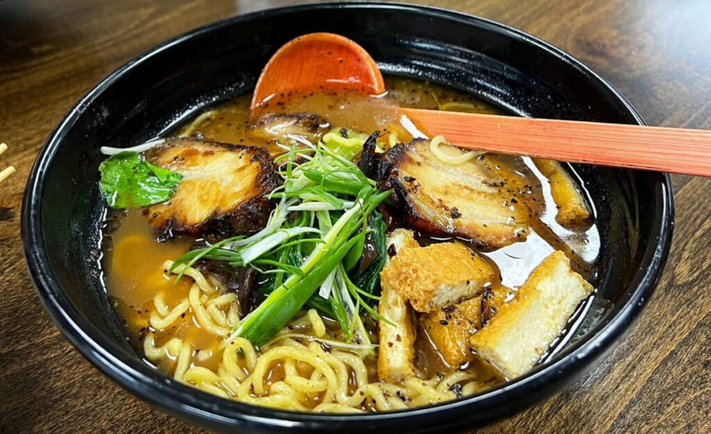 Featured article, "Soup In Asheville" image with large black bowl fill with ramen, including noodles, broth, tofu, and vegetables from Mizu Noodle and Asian Cuisine in Asheville, NC